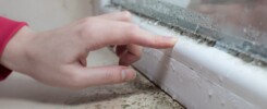 womans hand on leaking window just above mold growth on window ledge.